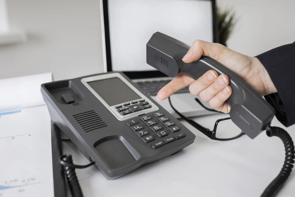 Hand holding a handset of a conference or office intercom phone on a desk, promoting intercom solutions in Kerala.