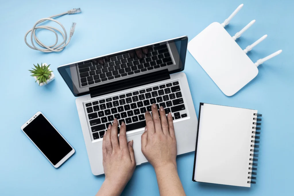 Workspace setup with a laptop, smartphone, Wi-Fi router, Ethernet cable, notebook, and a small plant, demonstrating professional network installation services in Kerala.