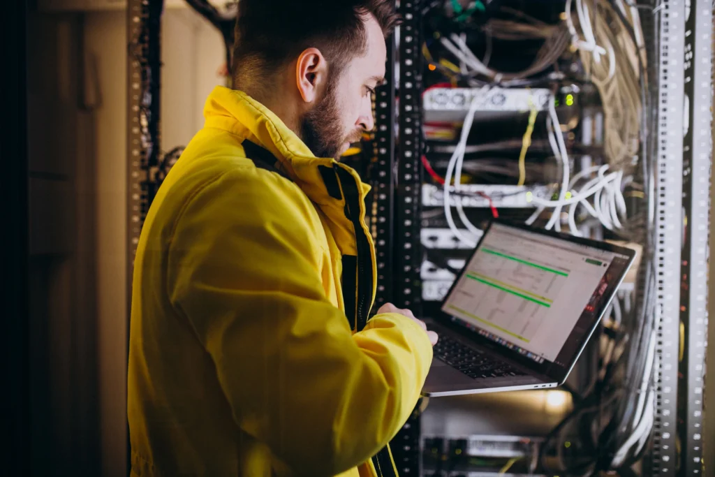 Network technician working on a laptop in a server room, demonstrating professional network installation services in Kerala
